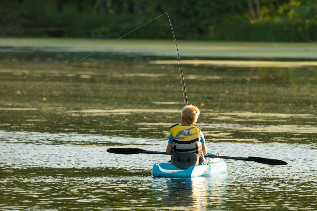 A young boy in a kayak fishing on a serene lake in Minnesota, enjoying an outdoor adventure.
